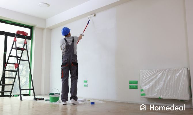 Imbianchino professionista che tinteggia una parete con rullo telescopico, durante un lavoro interno; esempio di intervento utile per valutare le tariffe imbianchino - Homedeal