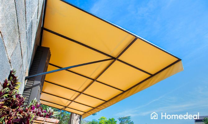 Tenda da sole gialla montata su una parete in pietra, che crea ombra su una terrazza soleggiata con vista su alberi e colline verdi - Homedeal