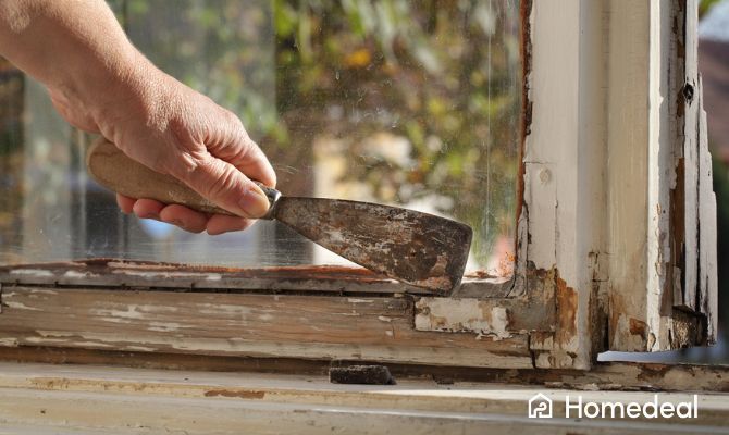 Restauro di vecchio infisso in legno danneggiato prima dell’installazione di doppi vetri, con spatola per rimuovere vecchio silicone e vernice deteriorata _ Homedeal