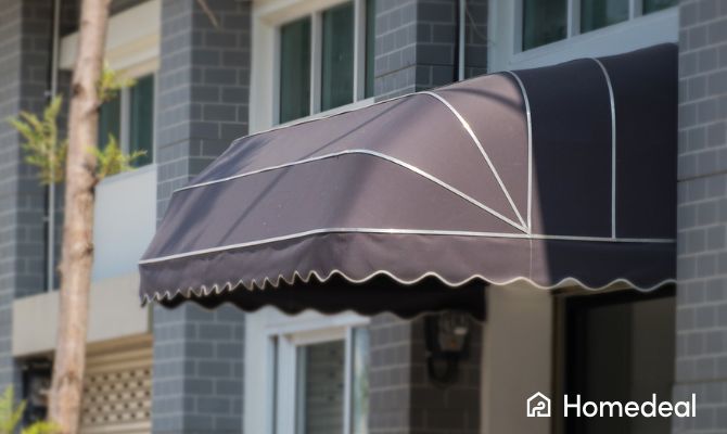 Tenda a cappottina nera installata sopra una finestra di un edificio moderno in mattoni grigi, con struttura in metallo e rifiniture decorative bianche - Homedeal