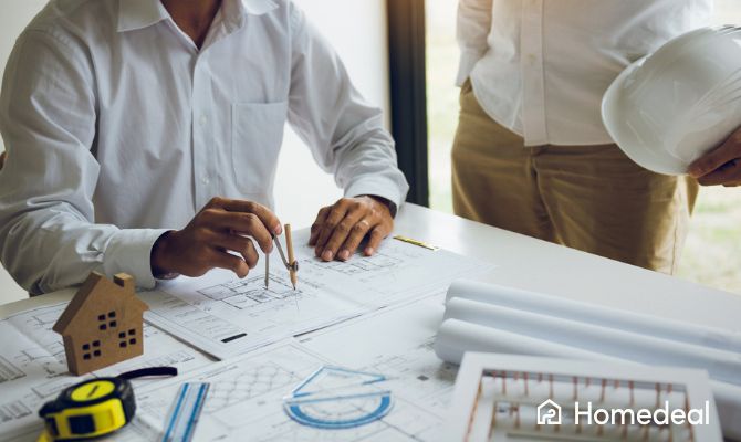 Incontro tra progettisti e tecnici su planimetrie per la costruzione di una casa da zero, con strumenti di misurazione, modelli e casco da cantiere – Homedeal
