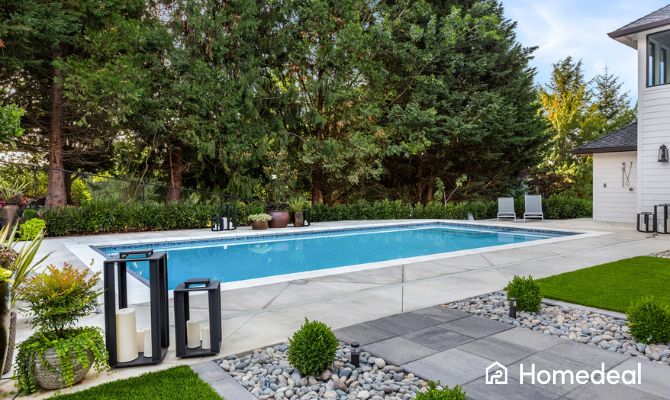 Piscina interrata moderna in un elegante giardino privato, circondata da piante sempreverdi, pavimentazione in cemento e decorazioni da esterno - Homedeal